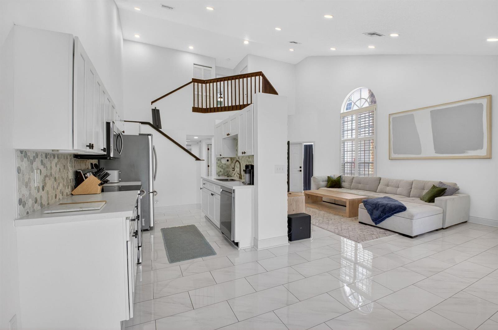 A modern open-concept kitchen and living area with white cabinetry, tile flooring, and vaulted ceilings — 5111 Sabal Gardens Lane # 4, Boca Raton FL 33487, BOCA RATON, FL