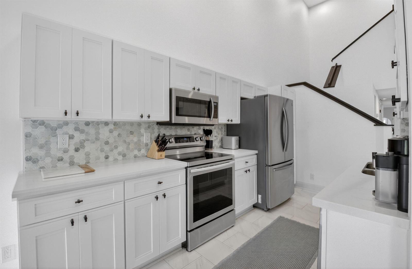 A kitchen features white cabinets, stainless steel appliances, a hexagonal tile backsplash, and white countertops — 5111 Sabal Gardens Lane # 4, Boca Raton FL 33487, BOCA RATON, FL