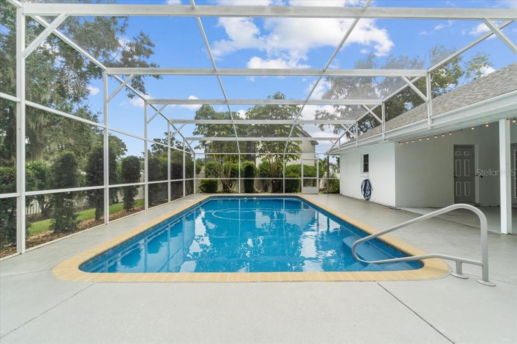 A rectangular swimming pool is enclosed by a screened lanai with a concrete deck — 725 HERITAGE DRIVE NE, WINTER HAVEN, FL
