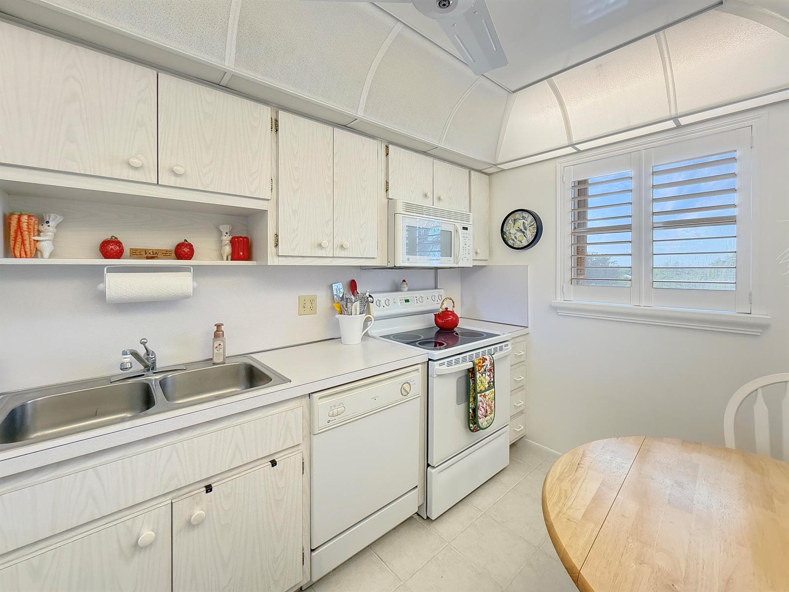 A kitchen features white wood-grain cabinets, white appliances, a double sink, and a round table — 555 NW 4th Avenue # 401, Boca Raton FL 33432, BOCA RATON, FL
