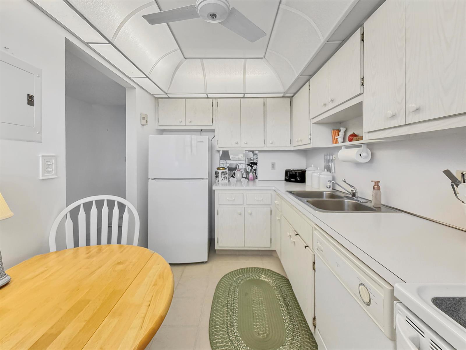 A kitchen features white cabinets, white appliances, a double sink, and a wooden dining table — 555 NW 4th Avenue # 401, Boca Raton FL 33432, BOCA RATON, FL