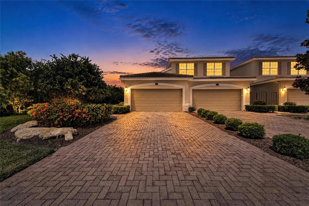 A paved driveway leads to the two-car garage of a two-story home at dusk — 419 WINDING BROOK LANE UNIT 101, BRADENTON, FL