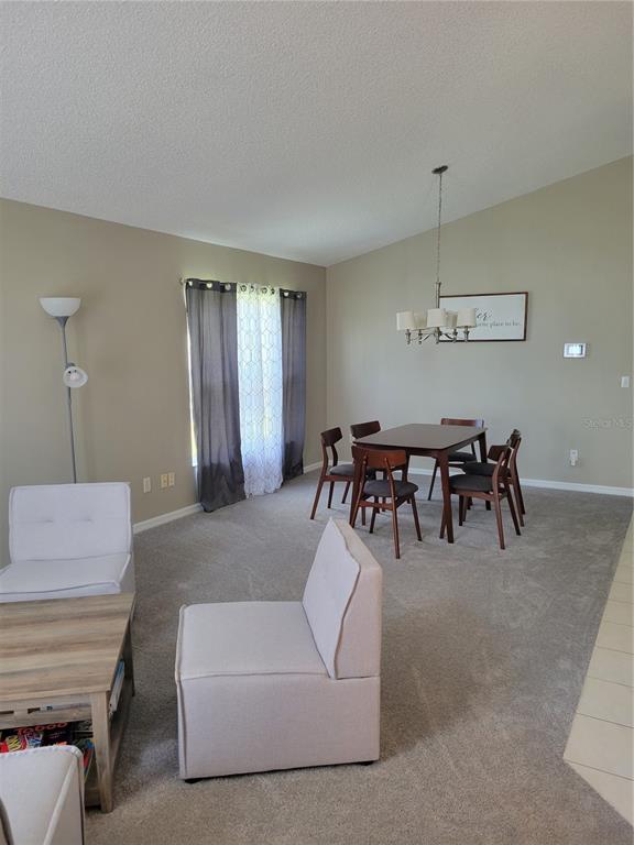 A dining area with a wooden table and chairs sits next to a carpeted living space — 1310 SEASONS BOULEVARD, KISSIMMEE, FL