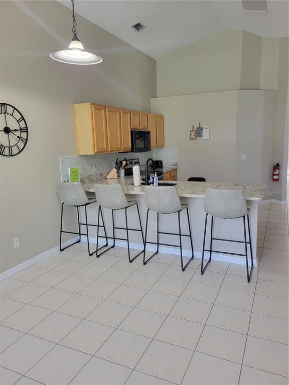 A kitchen features light wood cabinets, granite countertops, a breakfast bar with four stools, and tile flooring — 1310 SEASONS BOULEVARD, KISSIMMEE, FL