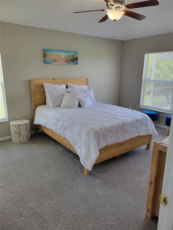 A bedroom features a wooden bed frame, white bedding, a ceiling fan, and carpeted floors — 1310 SEASONS BOULEVARD, KISSIMMEE, FL