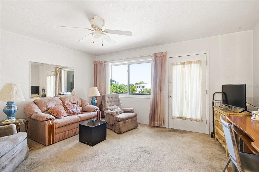 A living room features a sofa, recliner, ceiling fan, carpeted floors, and a glass-paneled door — 8126 112TH STREET UNIT 306, SEMINOLE, FL