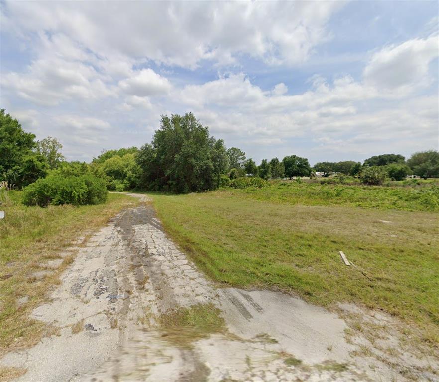 A cracked asphalt path leads through an open, grassy field toward a cluster of trees — 390 SHEPPARD ROAD NW, LAKE PLACID, FL