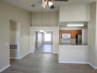 A living area with light wood-look flooring leads to a kitchen with a breakfast bar — 14905 Pleasant Bay Lane # 6204, Naples FL 34119, NAPLES, FL