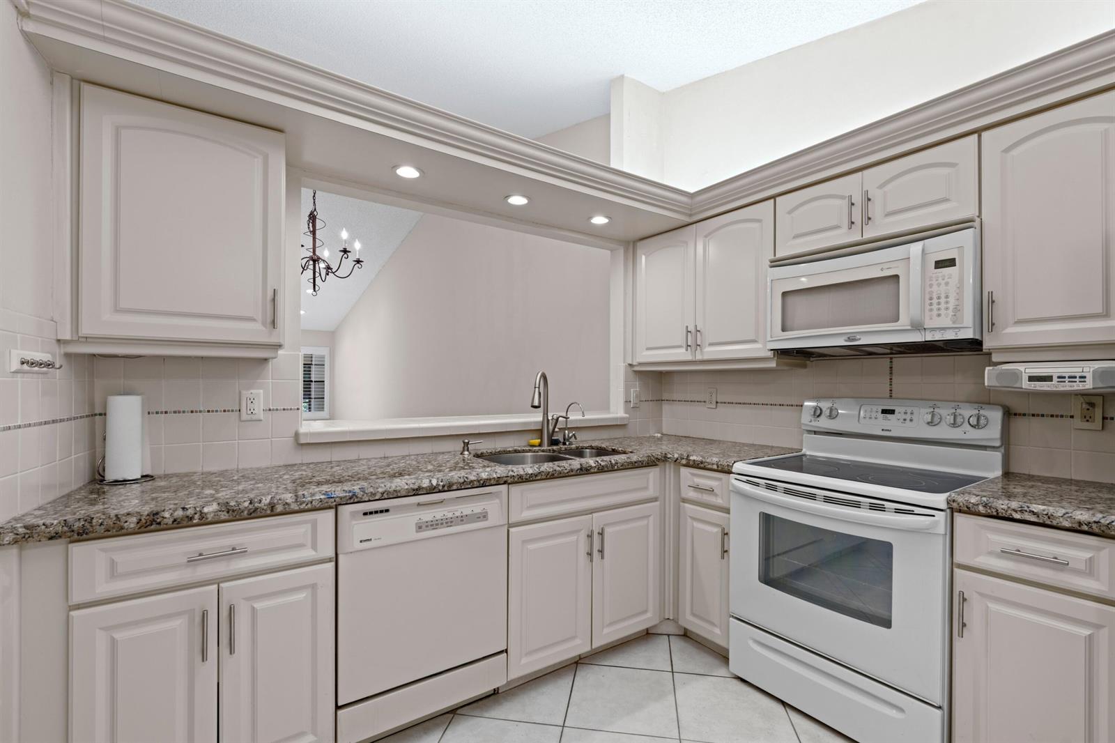 A kitchen with light-colored cabinets, granite countertops, white appliances, and a pass-through window — 10044 Andrea Lane # A, Boynton Beach FL 33437, BOYNTON BEACH, FL