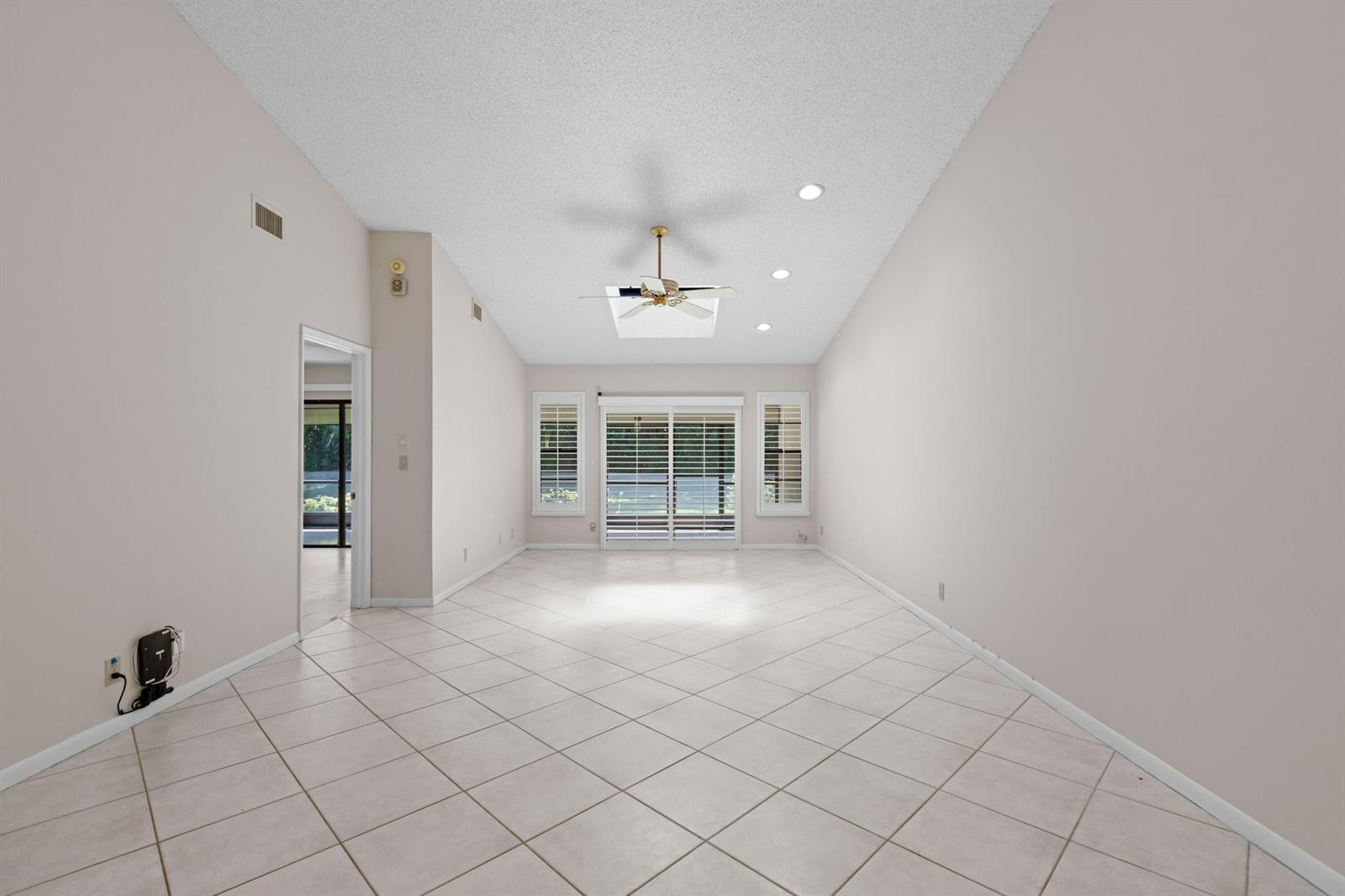 An empty living room with vaulted ceilings, tile floors, a ceiling fan, and sliding doors — 10044 Andrea Lane # A, Boynton Beach FL 33437, BOYNTON BEACH, FL