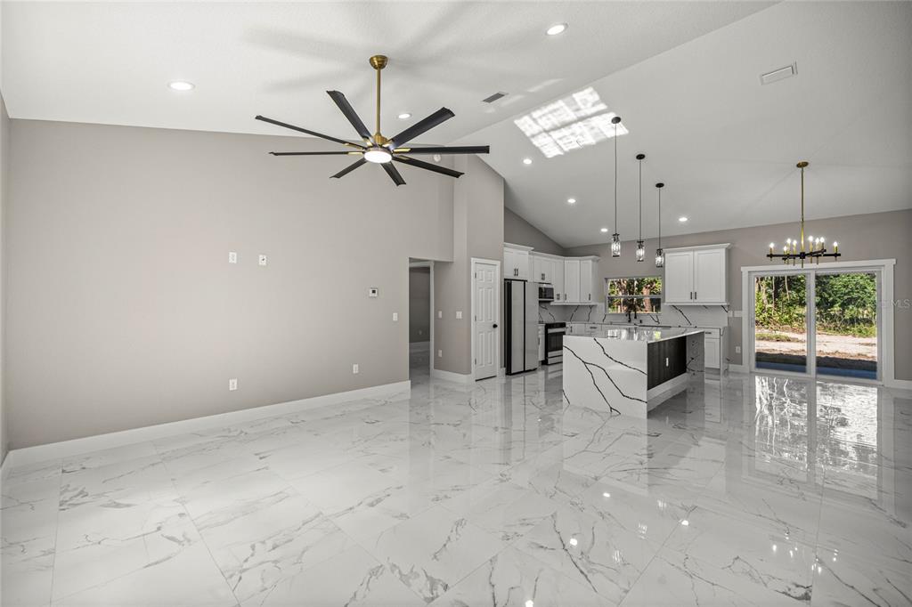 An open-concept living area features white marble-look tile flooring, a kitchen island, and vaulted ceilings — 3981 SE 142ND LANE, SUMMERFIELD, FL
