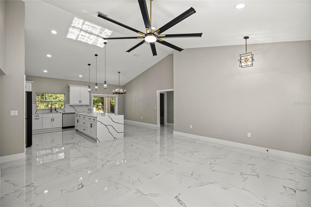 A modern kitchen and dining area feature white marble floors, a large island, and vaulted ceilings — 3981 SE 142ND LANE, SUMMERFIELD, FL