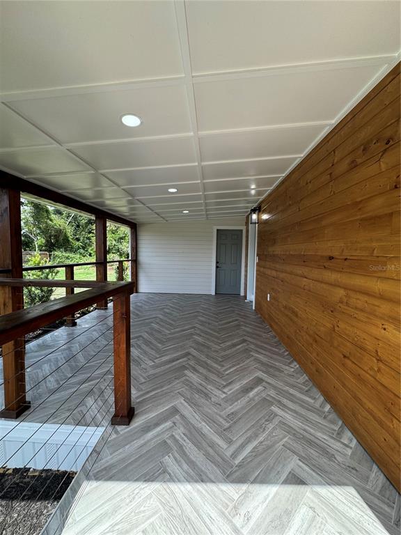 A covered porch features a herringbone-patterned floor, wood-paneled wall, and recessed ceiling lighting — 1119 N PARSONS AVENUE, SEFFNER, FL