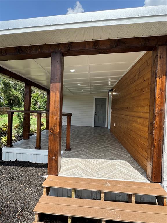 A covered outdoor patio features herringbone-patterned wood-look tile flooring and a wooden railing — 1119 N PARSONS AVENUE, SEFFNER, FL