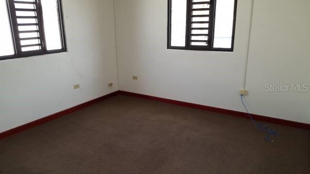 An empty room features brown carpet, white walls, dark trim, and two windows with shutters — 204 GUAYAMA, SAN JUAN, PR