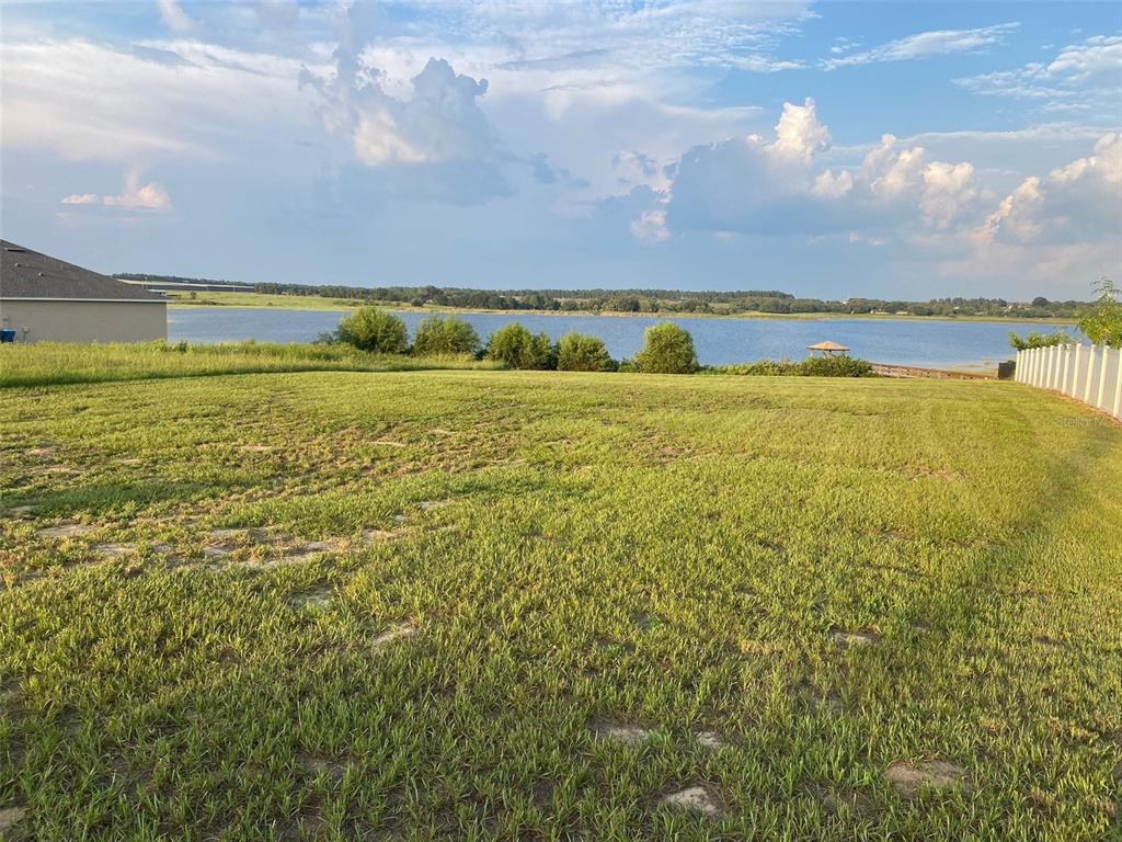 A grassy backyard overlooks a large lake under a cloudy blue sky — 4712 BROOKSHIRE COURT, LAKE WALES, FL
