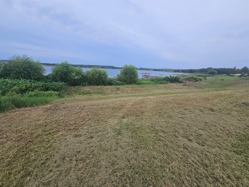 A grassy hill slopes down toward a lake with a small wooden pier — 4712 BROOKSHIRE COURT, LAKE WALES, FL