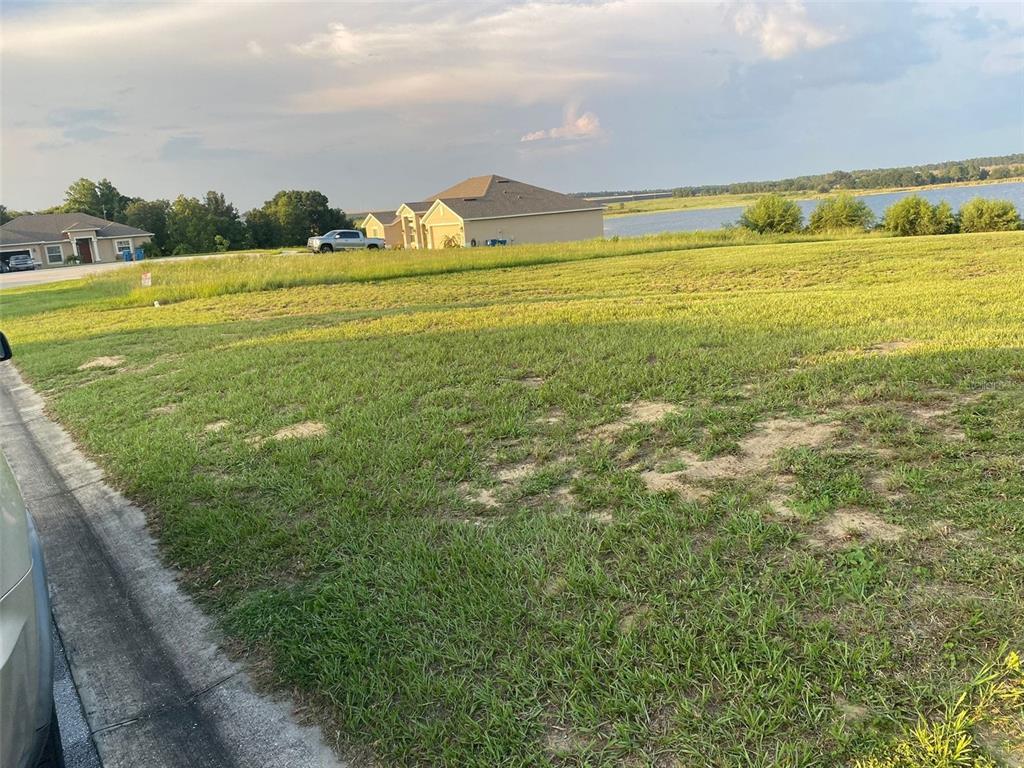 A vacant grassy lot sits in front of suburban houses with a lake in the distance — 4712 BROOKSHIRE COURT, LAKE WALES, FL