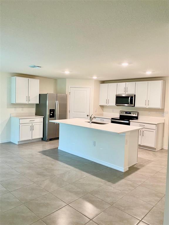A kitchen features white cabinets, stainless steel appliances, a center island, and tiled flooring — 10278 SE 161ST STREET, SUMMERFIELD, FL