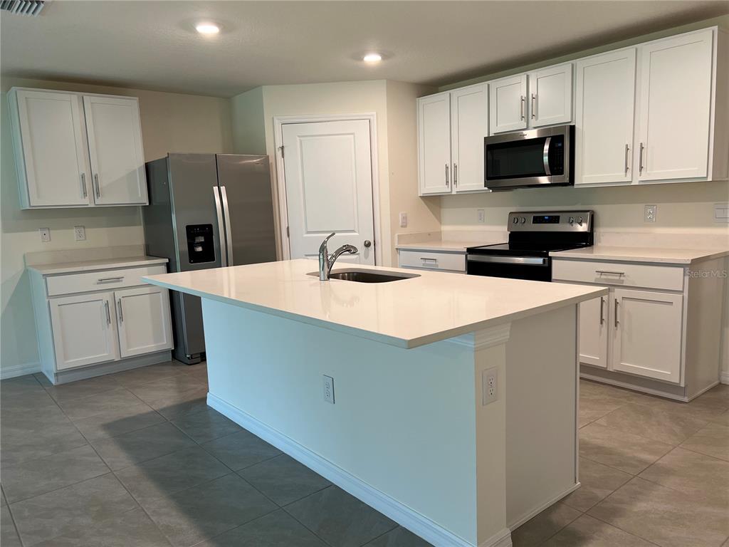 A kitchen features white cabinets, stainless steel appliances, a center island, and tile flooring — 10278 SE 161ST STREET, SUMMERFIELD, FL