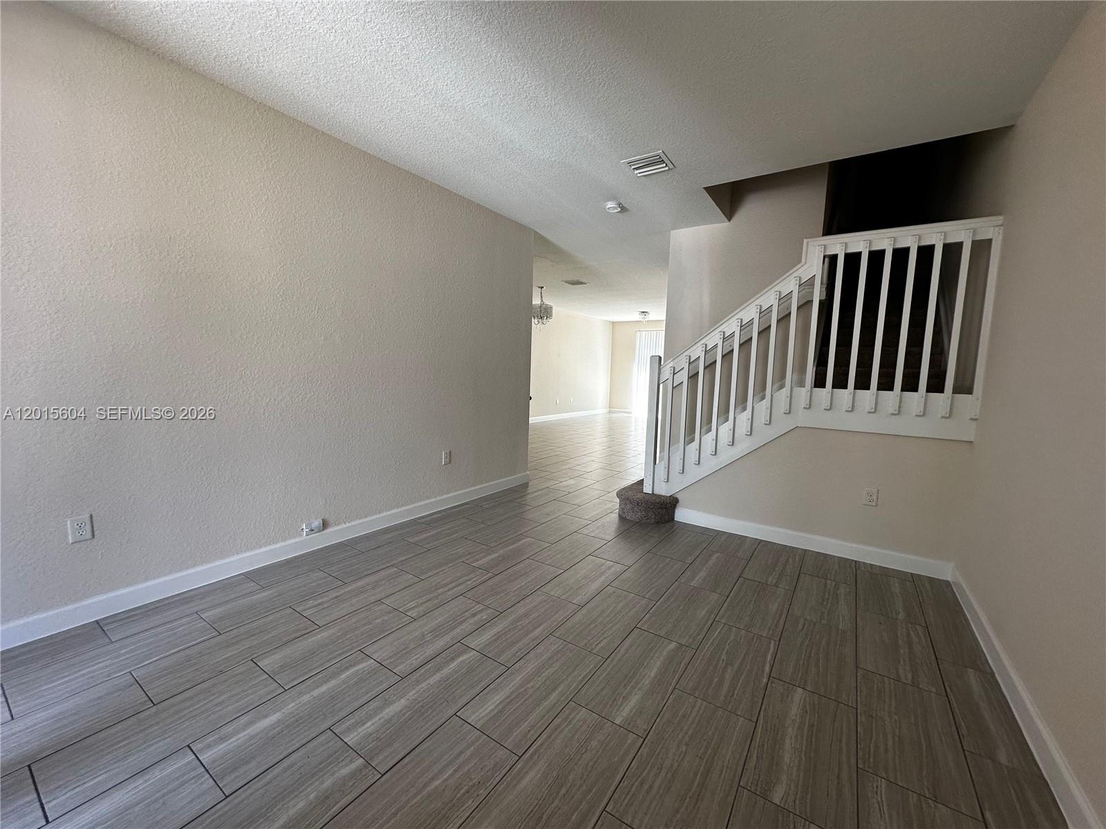 An empty room features light wood-look tile flooring, beige walls, and a white staircase railing — 1036 NE 208th St # 1036, Miami FL 33179, MIAMI, FL