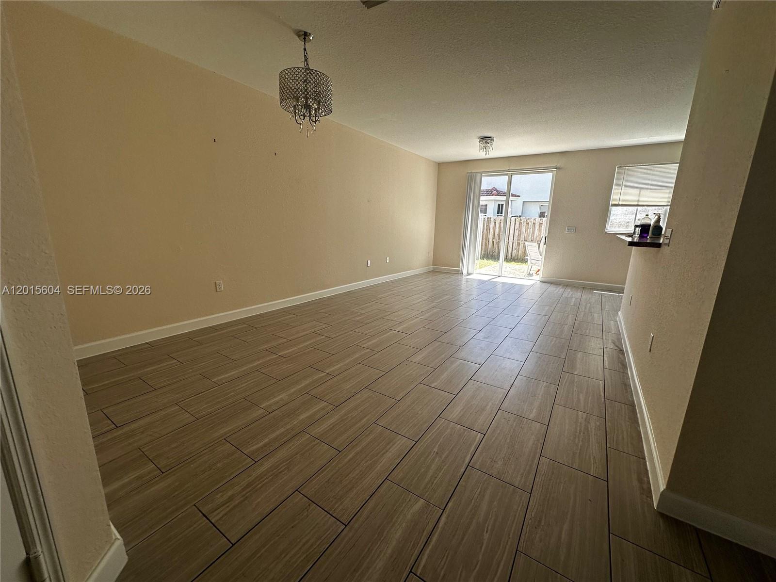 An empty living room features light-colored walls, wood-look tile flooring, and a sliding glass door — 1036 NE 208th St # 1036, Miami FL 33179, MIAMI, FL