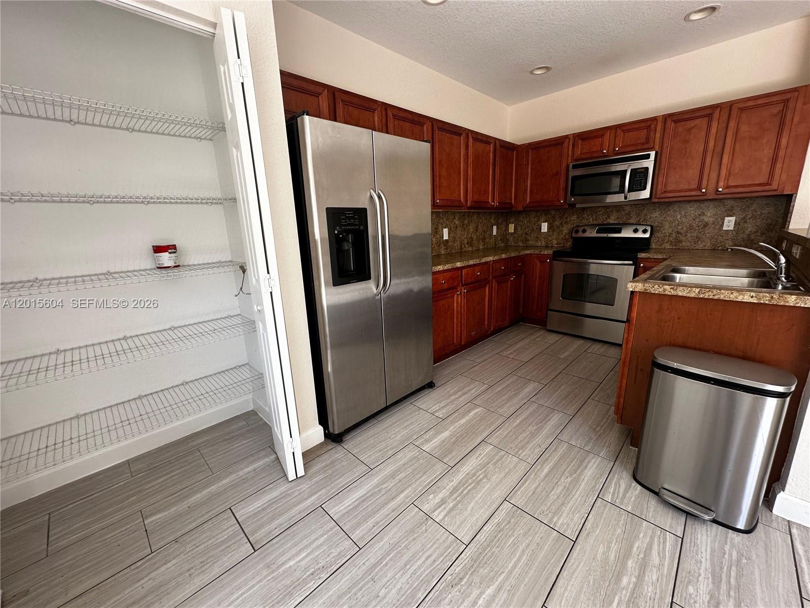 A kitchen features wood cabinets, stainless steel appliances, a pantry, and light-colored tile flooring — 1036 NE 208th St # 1036, Miami FL 33179, MIAMI, FL