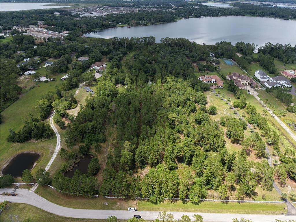 An aerial view shows a large, wooded lot with a pond and nearby residential houses — 0 CARSON STREET, ST CLOUD, FL