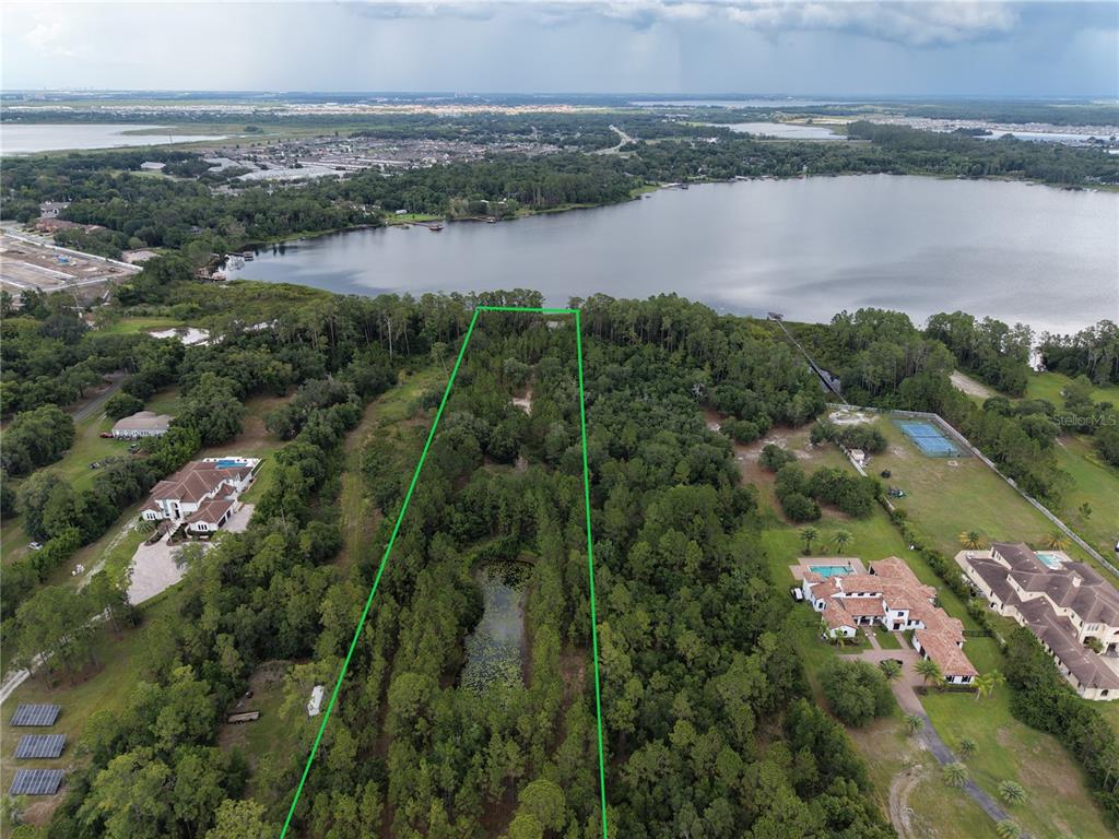 An aerial view shows a wooded lot with a pond, outlined in green, near a lake — 0 CARSON STREET, ST CLOUD, FL