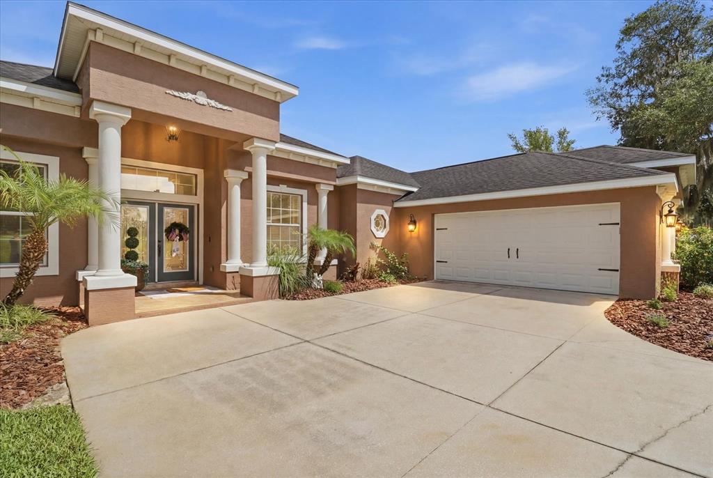 A tan single-story house features a white garage door and a covered entryway with columns — 3028 S DAVIS LAKE DRIVE, INVERNESS, FL