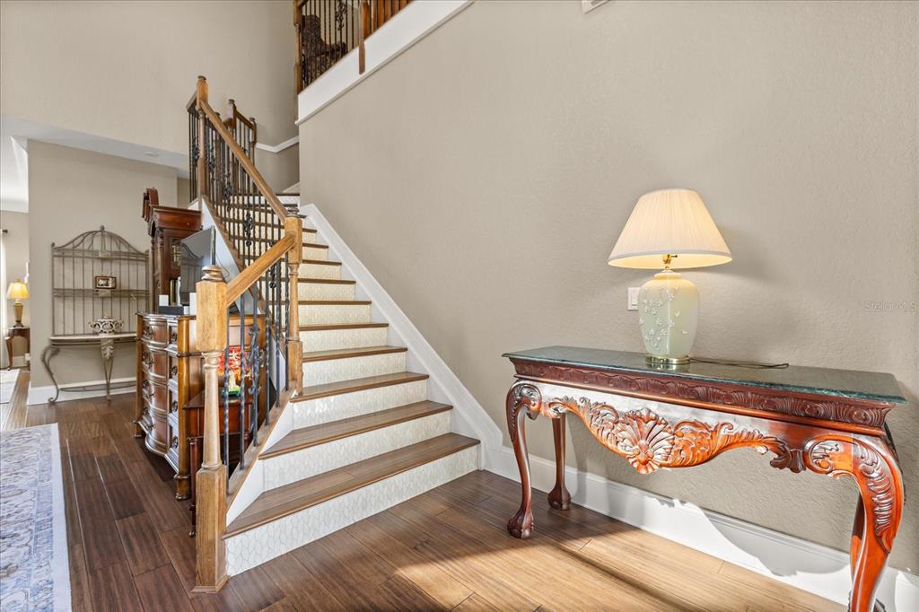 A staircase with wooden treads and patterned risers sits next to an ornate console table — 2450 DAHLGREN WAY, WINTER GARDEN, FL