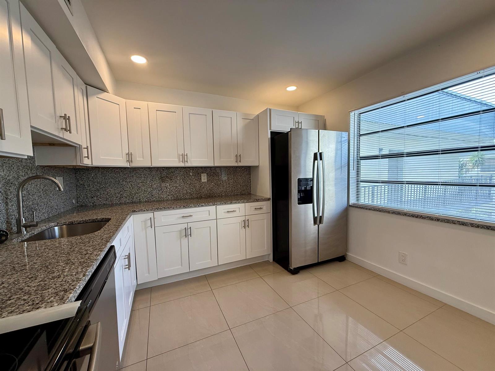 A kitchen features white cabinets, granite countertops, stainless steel appliances, and light-colored tile flooring — 514 Piedmont K, Delray Beach FL 33446, DELRAY BEACH, FL
