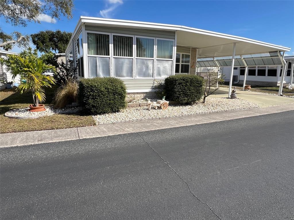 A single-story manufactured home features a large front window, a carport, and landscaped rock beds — 37 PINDO PALM STREET W, LARGO, FL