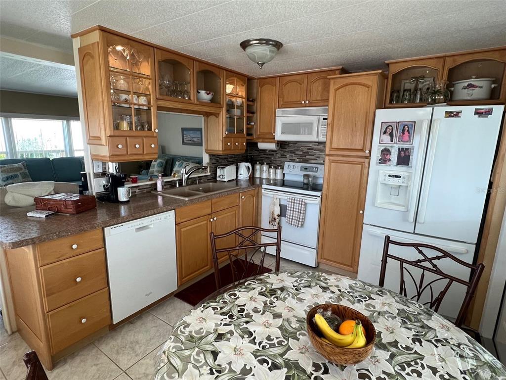 A kitchen features oak cabinets, white appliances, a tiled backsplash, and a round dining table — 37 PINDO PALM STREET W, LARGO, FL