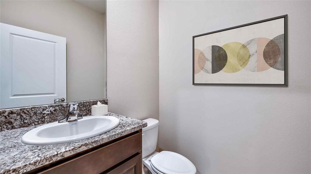 A half bathroom features a granite vanity countertop, a white sink, and wall-mounted artwork — 1124 CHASEHILL LANE, ZEPHYRHILLS, FL