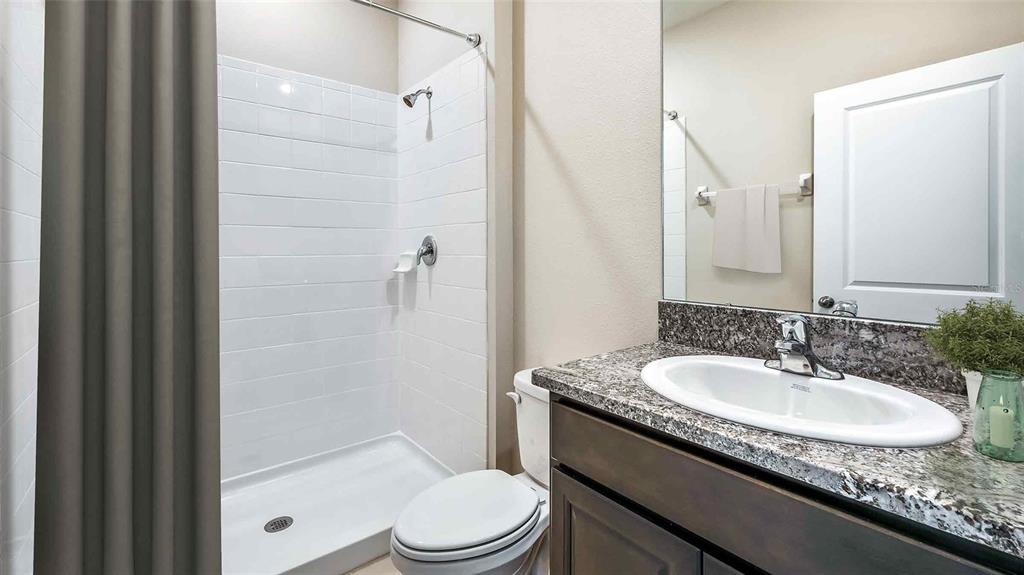 A bathroom features a tiled shower, a toilet, and a vanity with a granite countertop — 1124 CHASEHILL LANE, ZEPHYRHILLS, FL