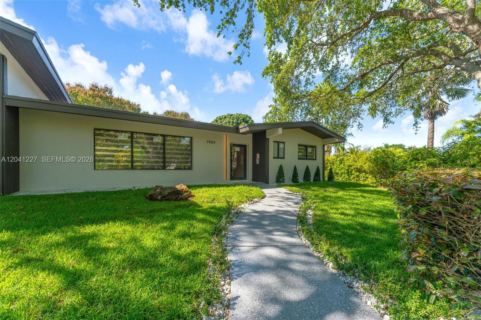 The exterior of a single-story house features a concrete walkway leading to the front entrance — 7920 SW 132nd St # 0, Pinecrest FL 33156, PINECREST, FL