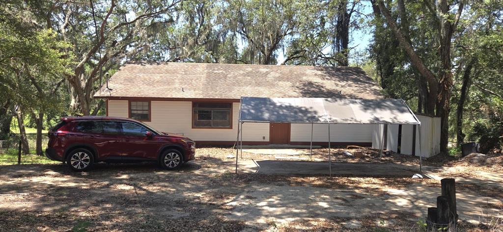 A red SUV is parked in front of a house with a metal carport canopy — 4322 CASAURINA ROAD, LADY LAKE, FL