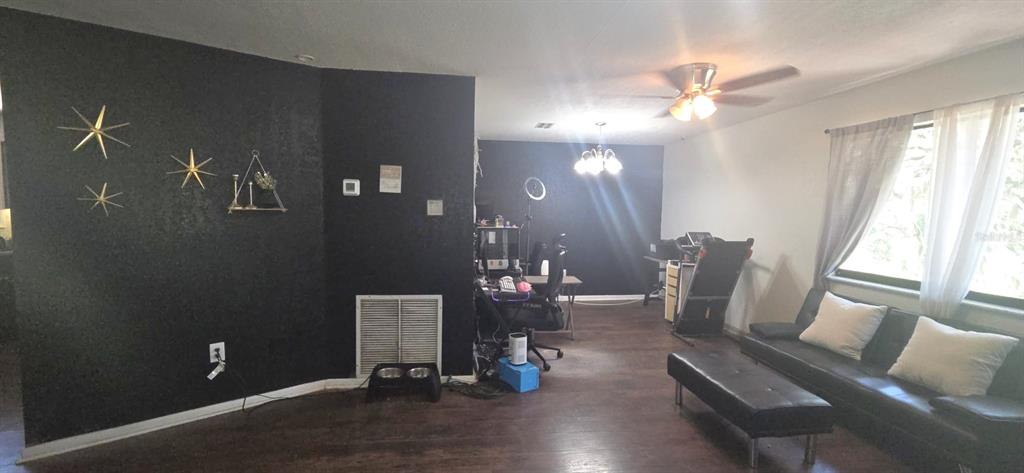 A living room features dark accent walls, wood-look flooring, a black sofa, and a treadmill — 4322 CASAURINA ROAD, LADY LAKE, FL