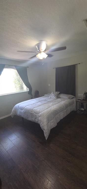 A bedroom features dark wood-look flooring, a ceiling fan, and a bed with a gray comforter — 4322 CASAURINA ROAD, LADY LAKE, FL