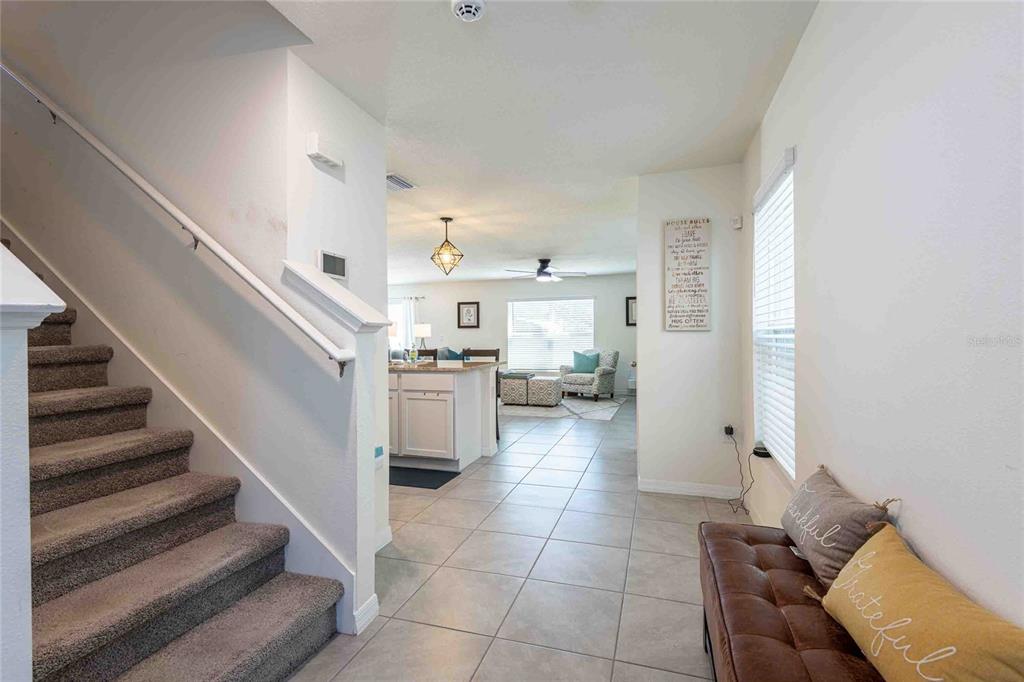 A carpeted staircase leads to an open-concept living area with tile flooring and a kitchen — 12172 LILY MAGNOLIA LANE, RIVERVIEW, FL