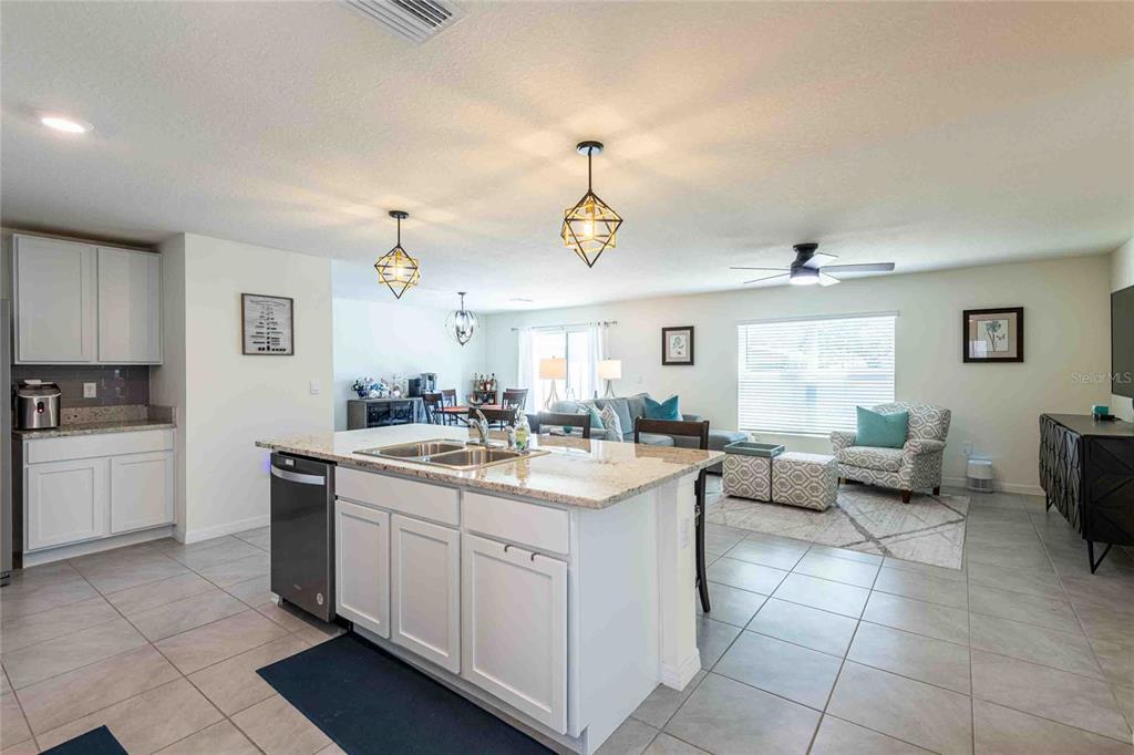 An open-concept kitchen with a granite island overlooks a living and dining area — 12172 LILY MAGNOLIA LANE, RIVERVIEW, FL