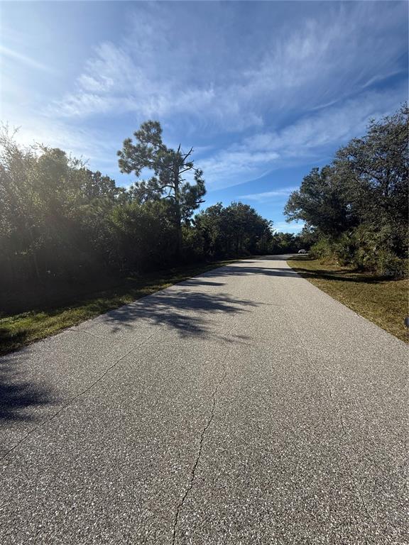A paved road stretches through a wooded area under a bright blue sky — 7358 PINEDALE DRIVE, PORT CHARLOTTE, FL