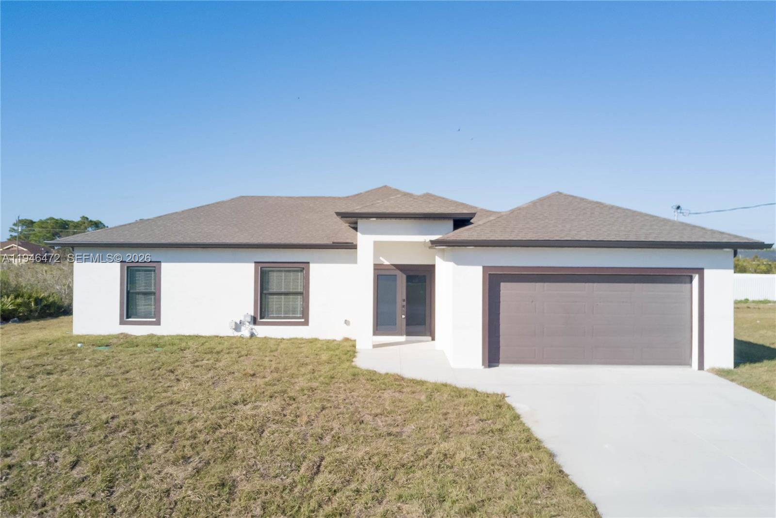A single-story white house with a brown roof, a two-car garage, and a concrete driveway — 3606 54TH ST W, Lehigh Acres FL 33971, LEHIGH ACRES, FL