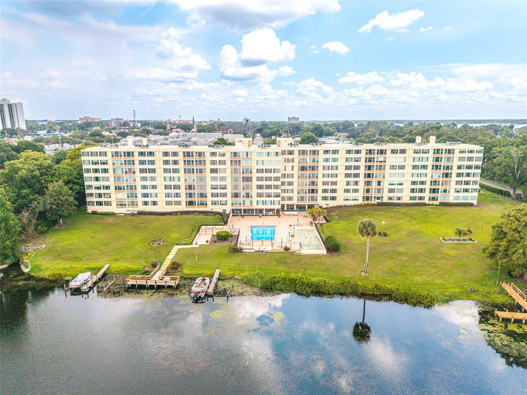 An aerial view shows a large apartment building with a pool and docks on a lake — 700 MIRROR TERRACE NW UNIT 511, WINTER HAVEN, FL