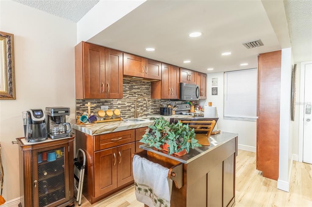 A kitchen features wood cabinets, a tiled backsplash, a central island, and light wood flooring — 700 MIRROR TERRACE NW UNIT 511, WINTER HAVEN, FL
