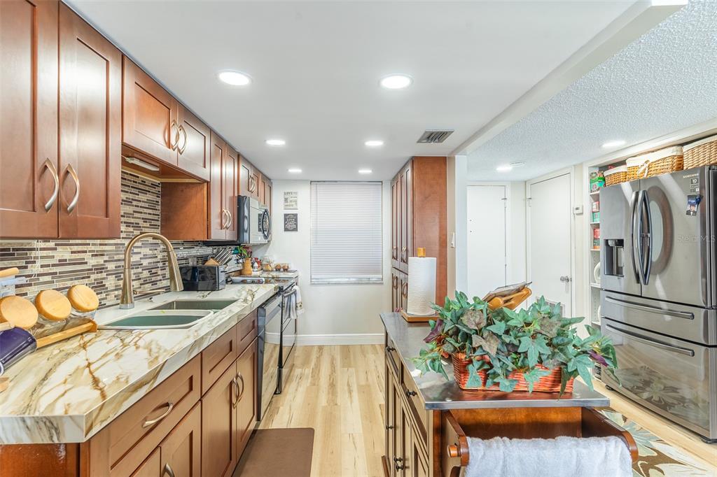 A kitchen features wood cabinets, a marble-patterned countertop, a stainless steel refrigerator, and recessed lighting — 700 MIRROR TERRACE NW UNIT 511, WINTER HAVEN, FL