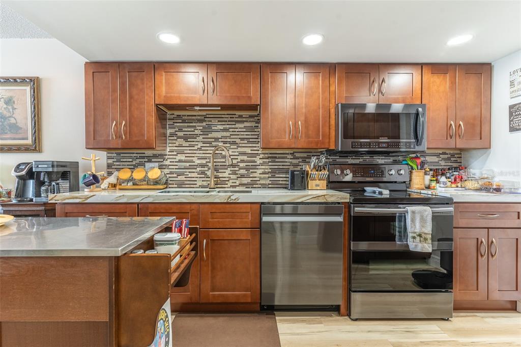 A kitchen features wood cabinets, stainless steel appliances, a tiled backsplash, and a metal island — 700 MIRROR TERRACE NW UNIT 511, WINTER HAVEN, FL