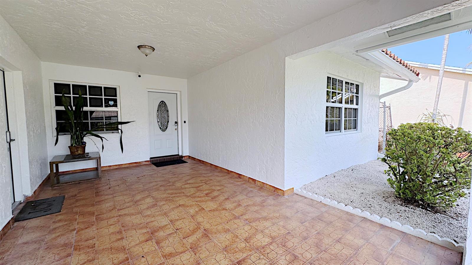 A covered patio features tiled flooring, white stucco walls, and a white front door — 411 SE 4th Street, Dania Beach FL 33004, DANIA BEACH, FL