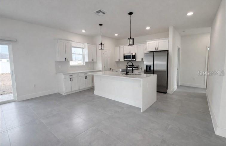 A modern kitchen features white cabinetry, a central island, stainless steel appliances, and gray tile flooring — 4837 SW 138TH LANE, OCALA, FL